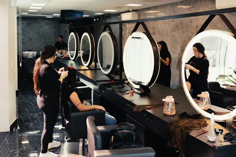 Stylists at work in front of round mirrors in a busy salon.